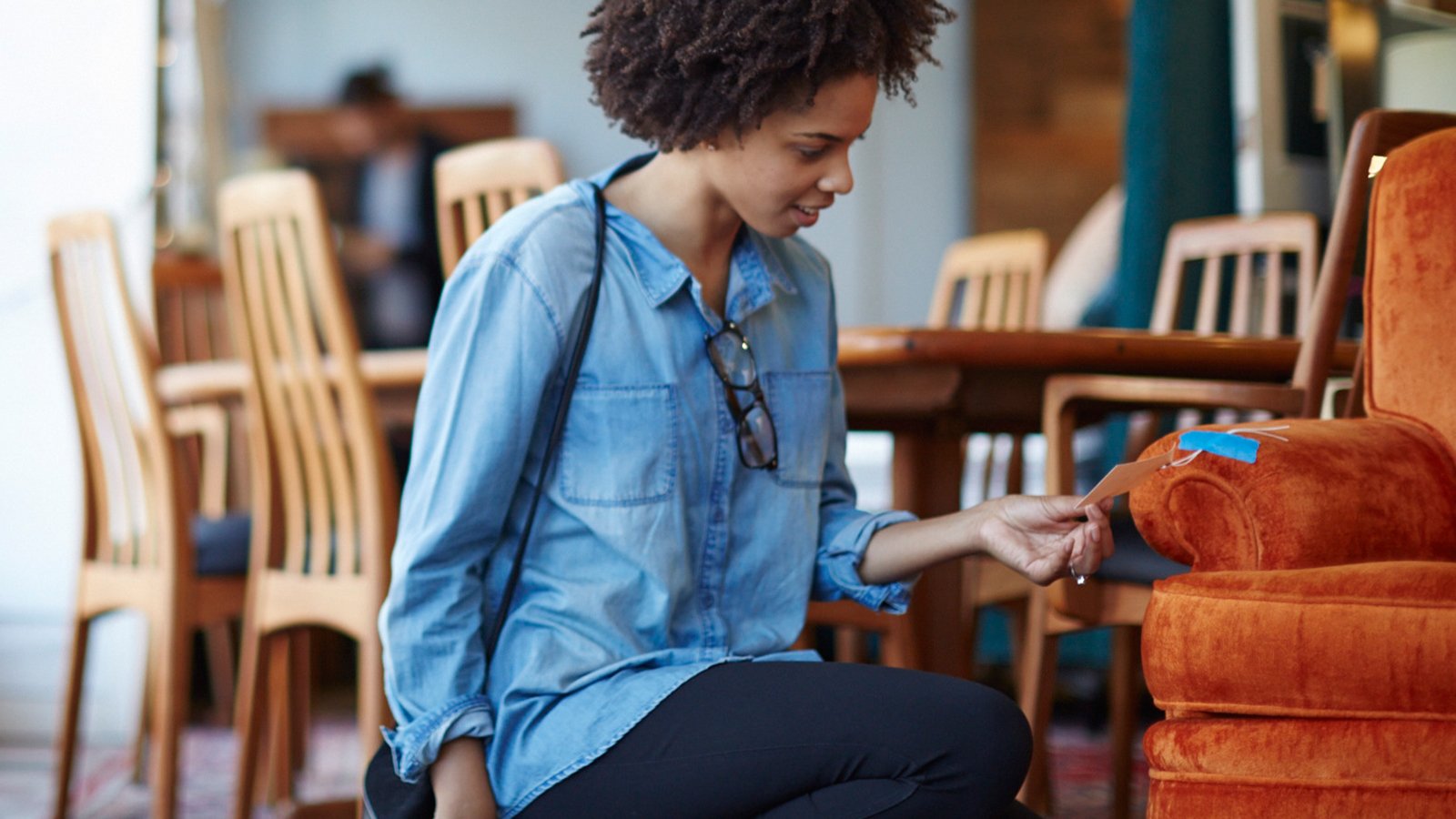 A woman kneeling in a furniture store looking at the price tag of a loveseat.