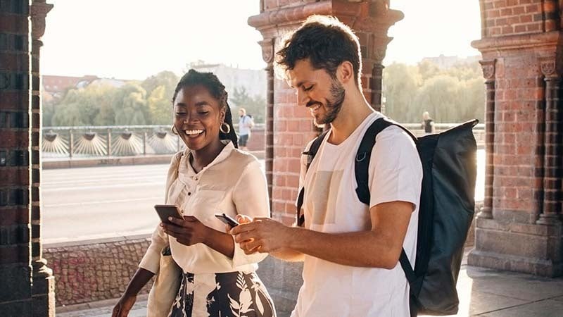 Mujer y hombre caminando mientras usan el teléfono