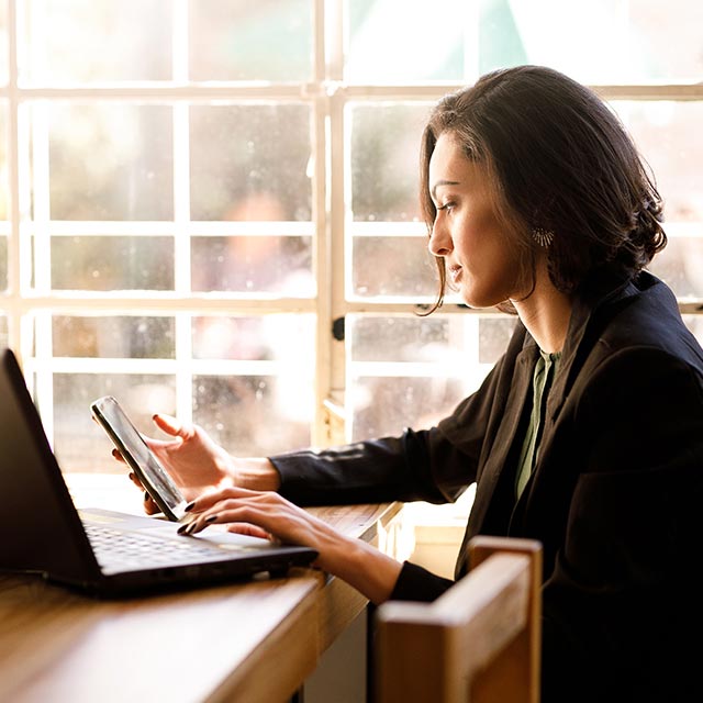 Mujer utilizando teléfono móvil y laptop